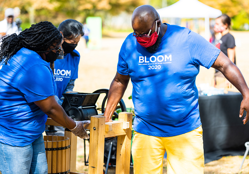 Two masked participants operating a cider press. BLOOM cider press in Jimi Hendrix Park, 2020. Photo courtesy of Dancing in the Rain. 
